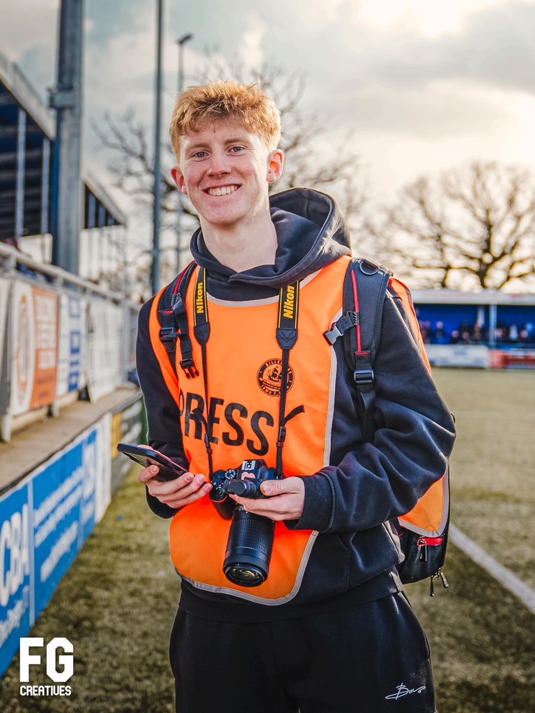 Flynn Gwilliams in a media bib holding his DSLR pitchside