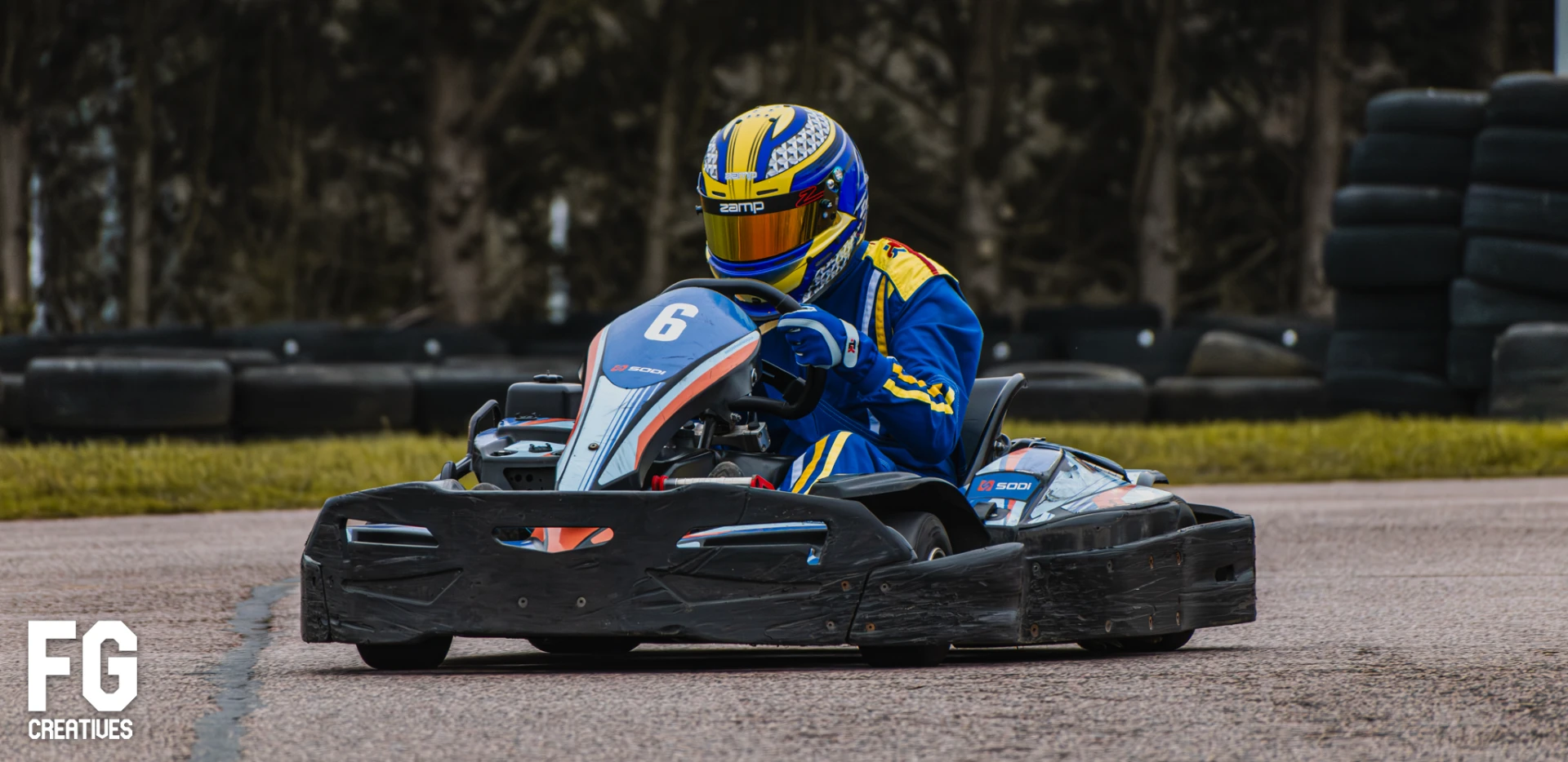 Kart driver number 6 in a blue and yellow helmet racing on track